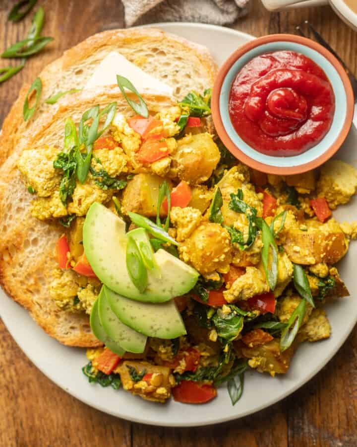 Plate of Tofu Scramble with toast, avocado slices, and a dish of ketchup.