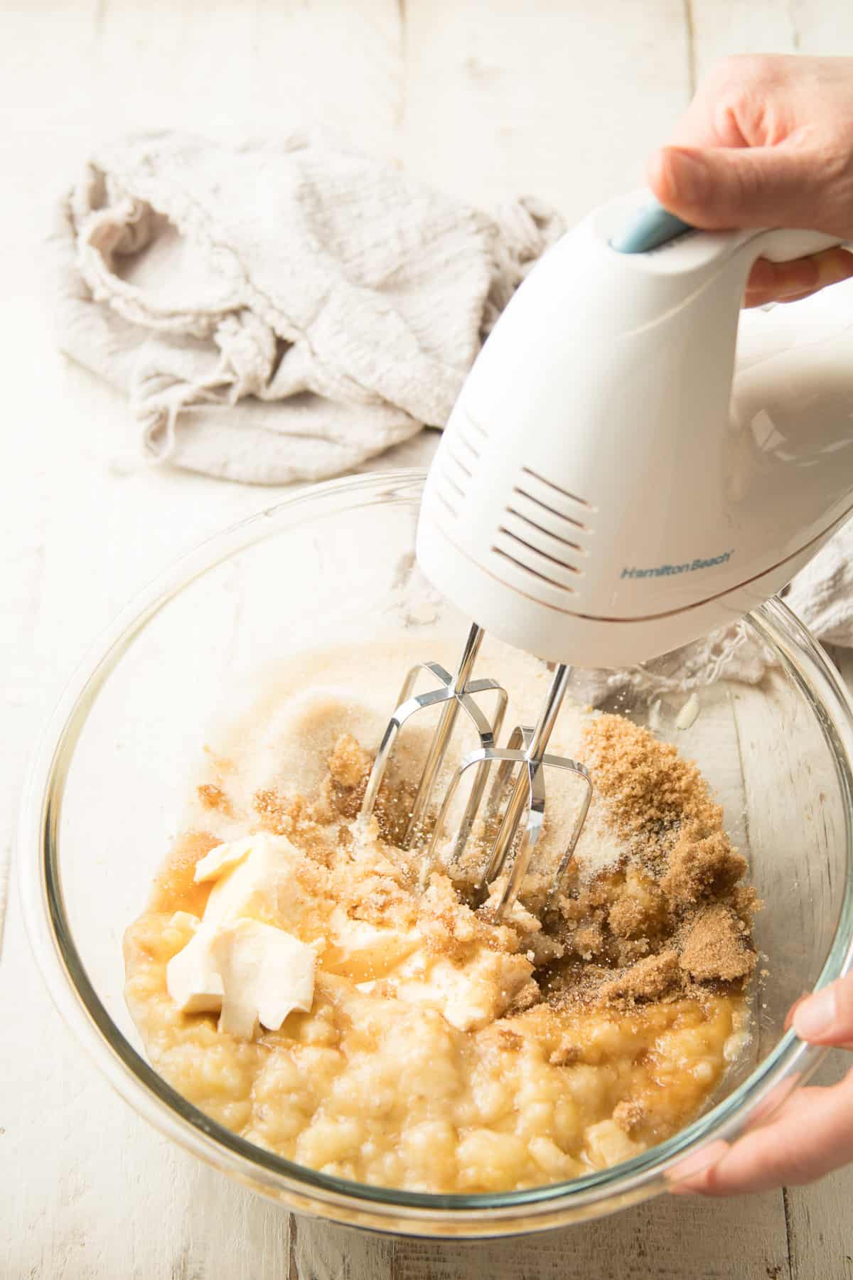 Hand beating bananas, butter, and sugar together with an electric mixer.