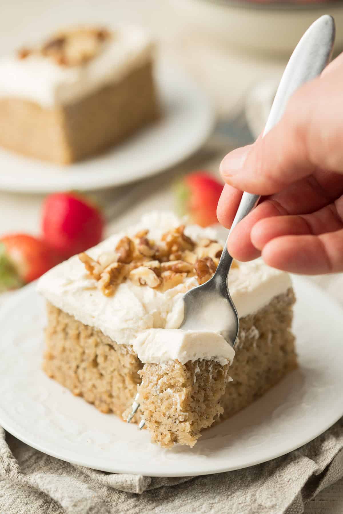 Hand scooping a bite of Vegan Banana Cake from a slice sitting on a plate.
