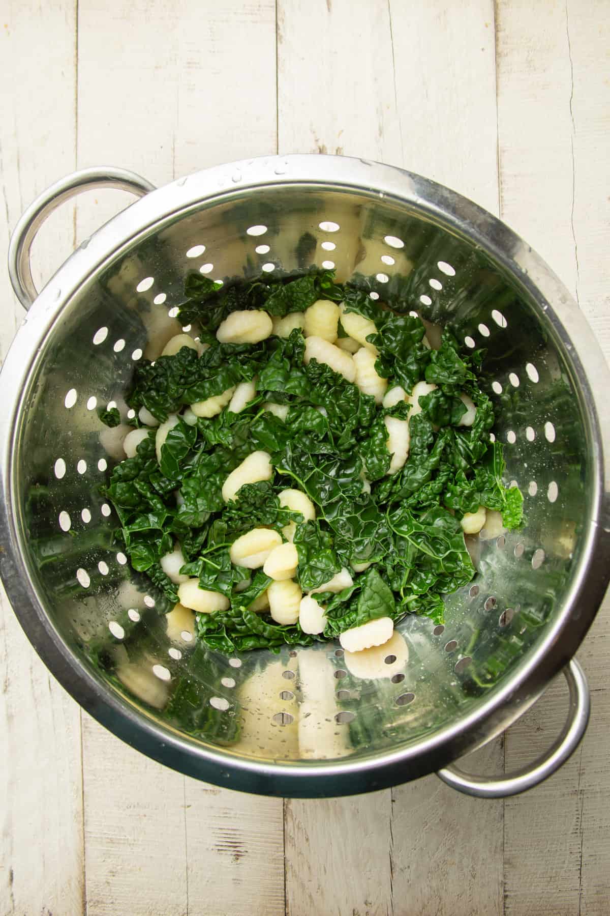 Colander filled with cooked potato gnocchi and kale.