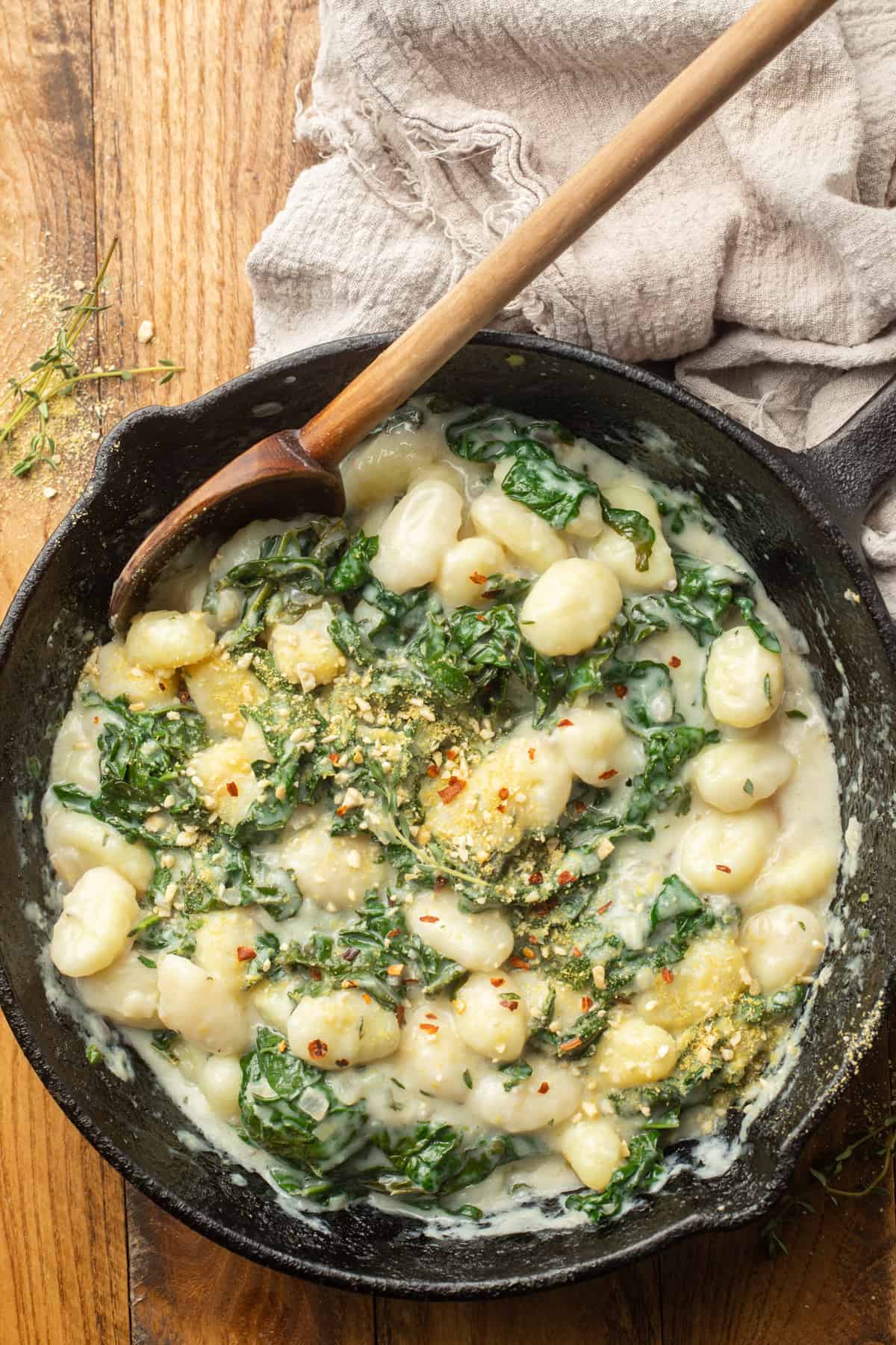 Skillet of vegan gnocchi and kale with wooden spoon.
