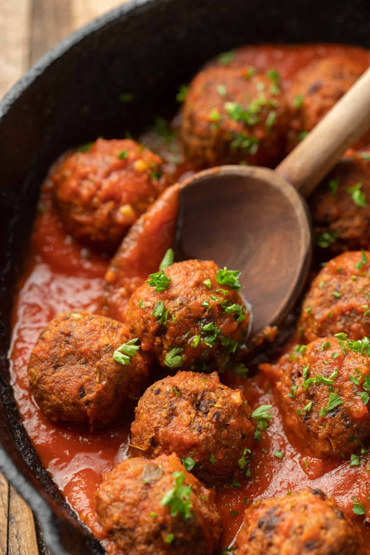 Wooden spoon scooping a Vegan Meatball from a skillet.