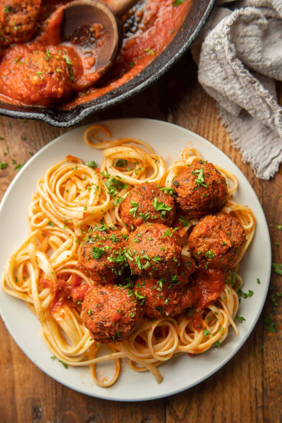 White wooden surface set with skillet and plate of spaghetti and Vegan Meatballs.