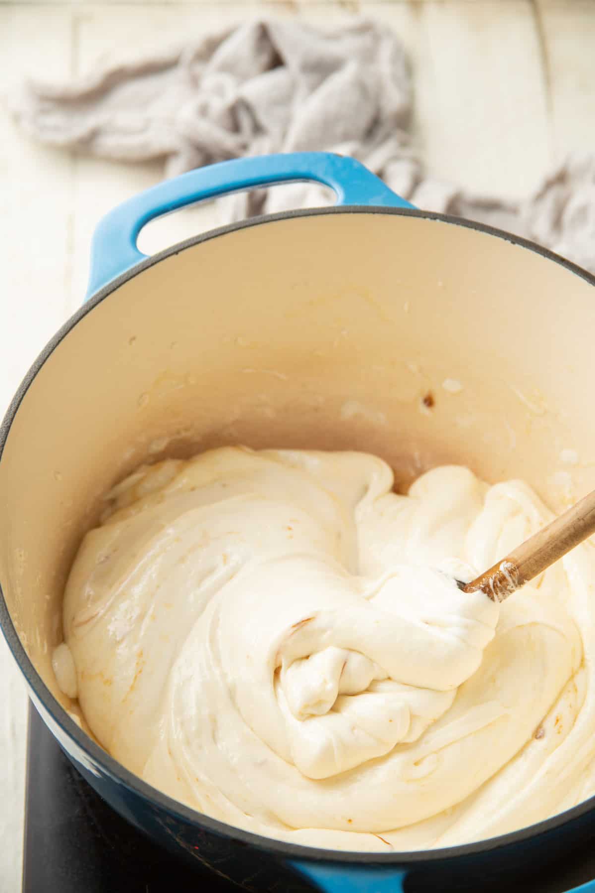 Wooden spoon stirring butter and melted marshmallows in a large pot.