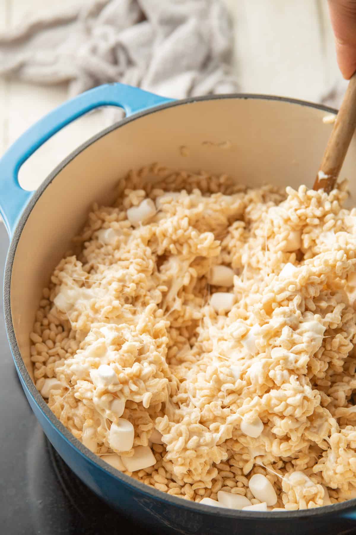 Spoon stirring crisp rice cereal into melted marshmallow mixture in a pot.