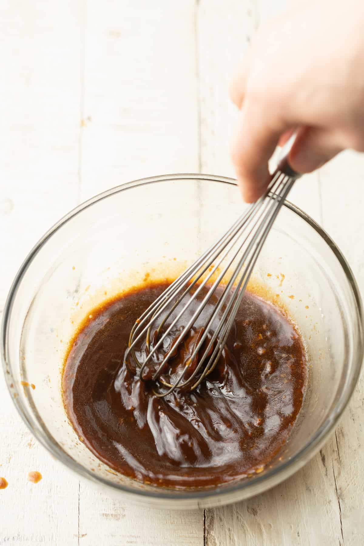 Hand whisking stir-fry sauce in a glass bowl.