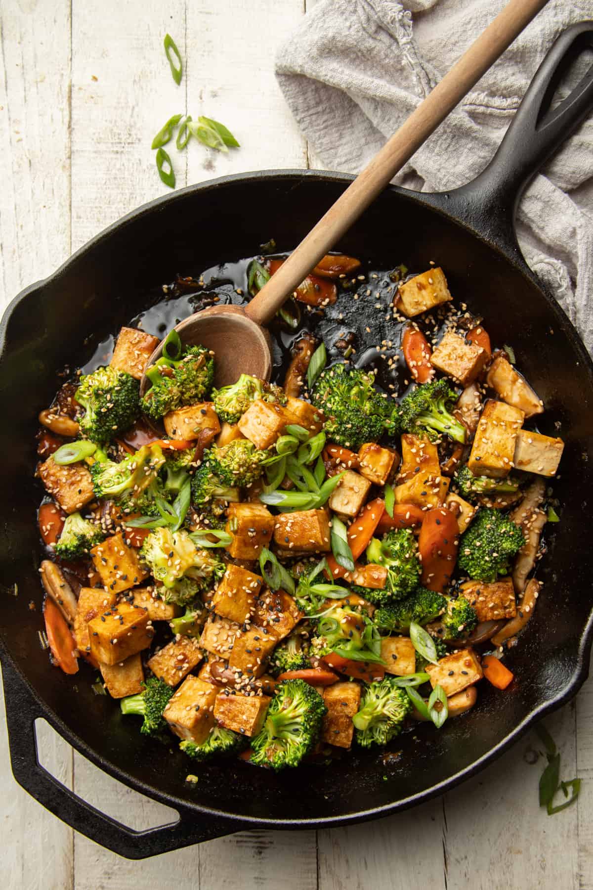 Skillet of Tofu Stir-Fry with wooden spoon on a white wooden surface.