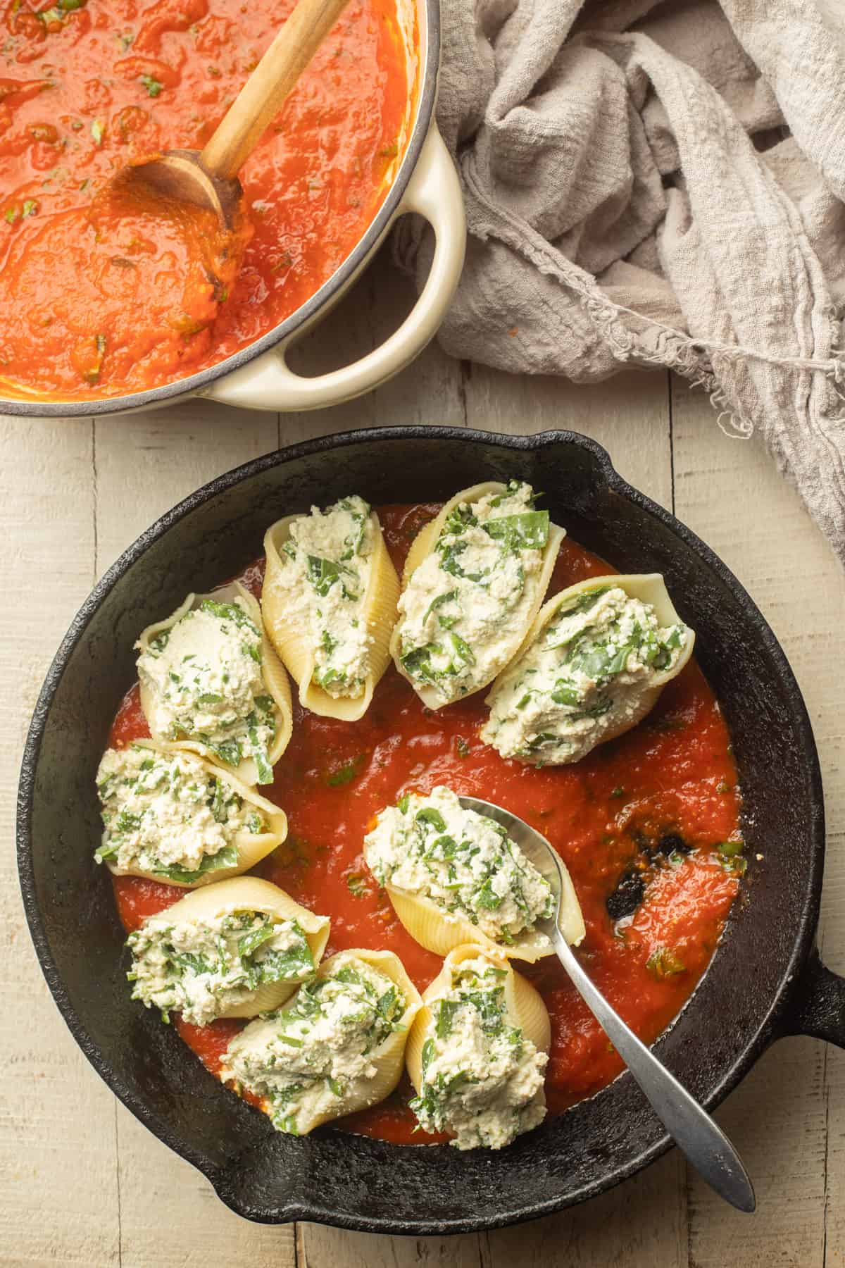 Skillet filled with tomato sauce and uncooked vegan stuffed shells.