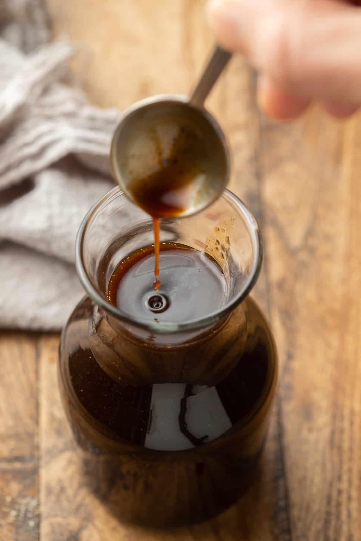 Hand drizzling Vegan Worcestershire Sauce into a bottle.