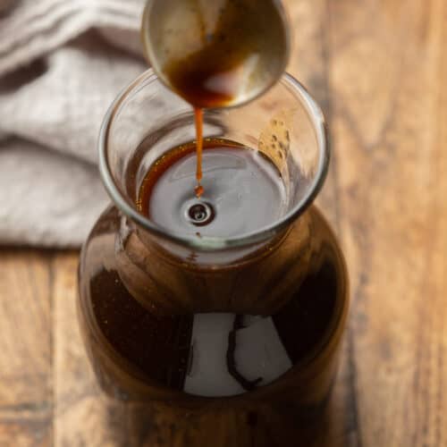 Close up of a spoon drizzling Vegan Worcestershire Sauce into a bottle.