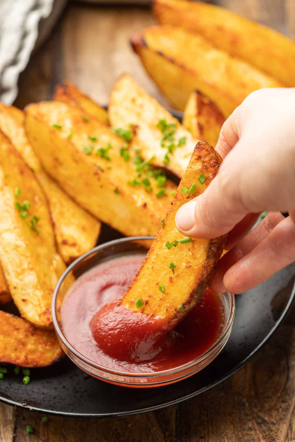 Hand dipping an Air Fryer Potato Wedge in a dish of ketchup.