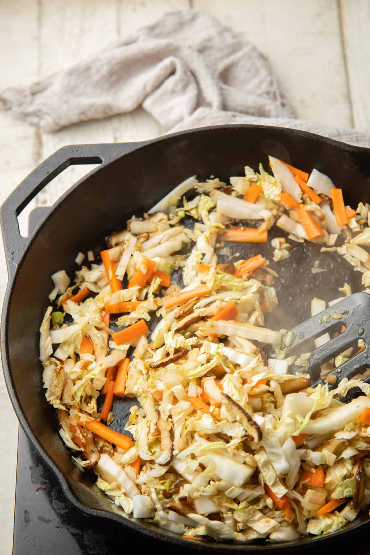 Cabbage, carrots, and mushrooms cooking in a skillet.