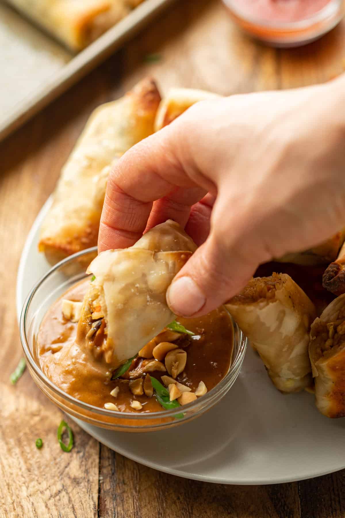 Hand dipping half of a spring roll into a dish of peanut sauce.