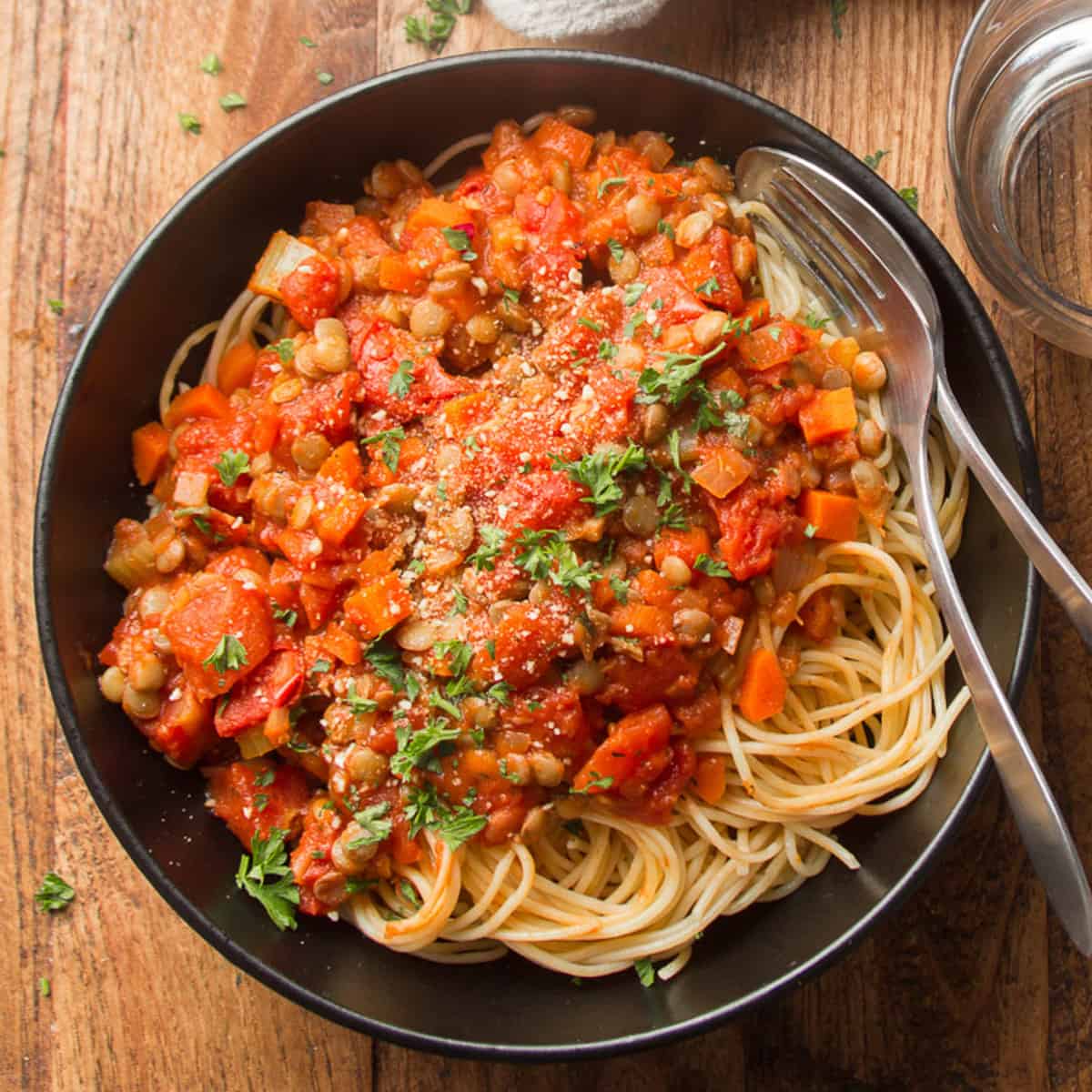 Plate of spaghetti topped with Lentil Bolognese and vegan parmesan cheese.