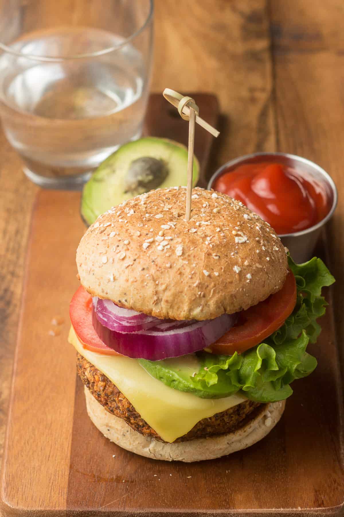 Quinoa burger with avocado, glass of water, and dish of ketchup in the background.