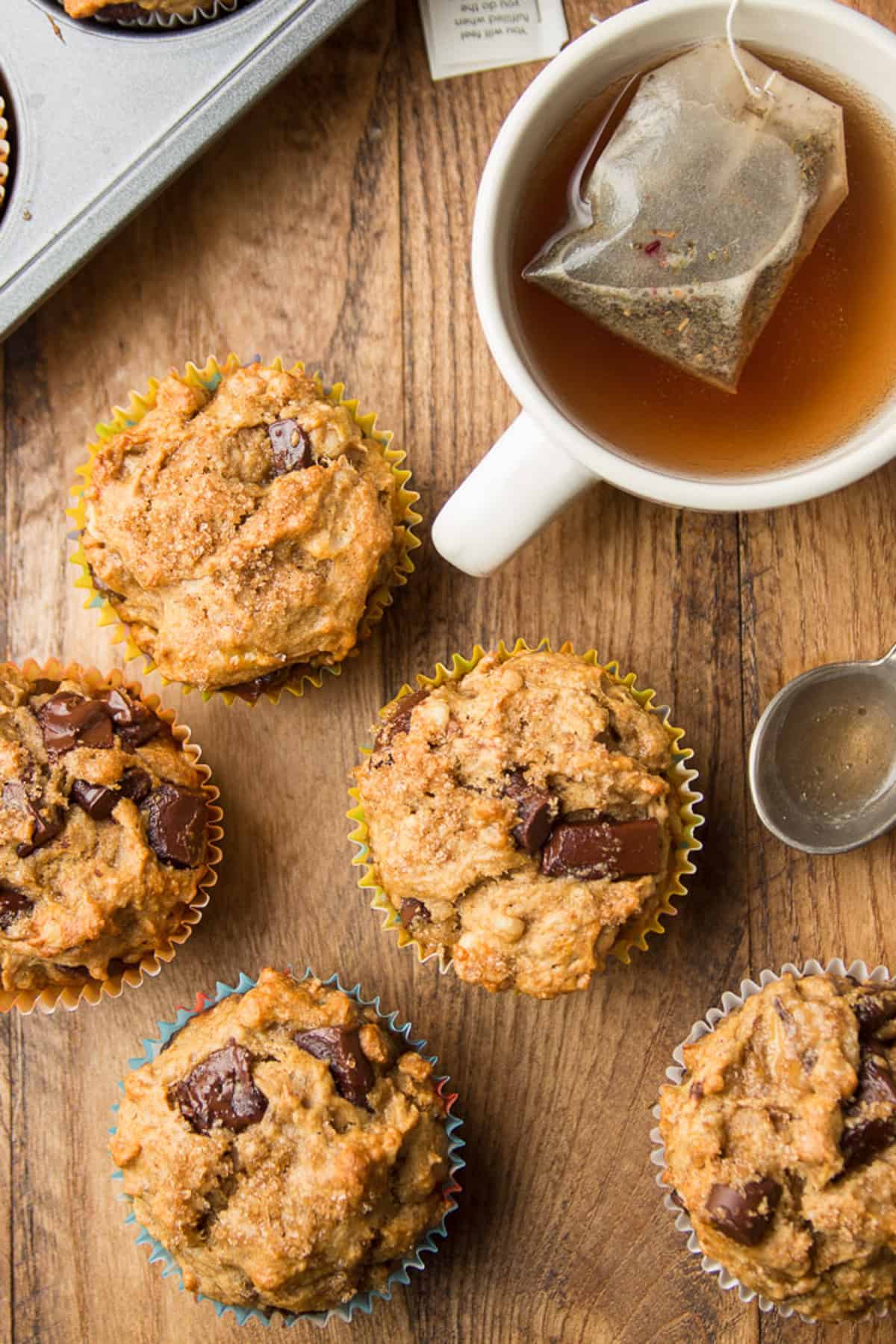 Vegan Banana Muffins on a wooden surface with cup of tea and spoon.