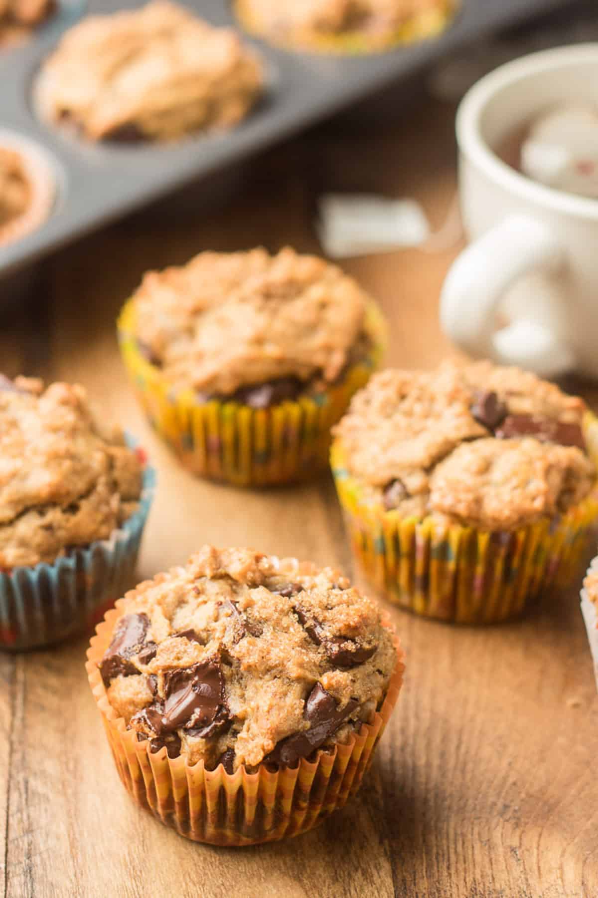 Vegan banana muffins with a tin of muffins and a cup of tea in the background.