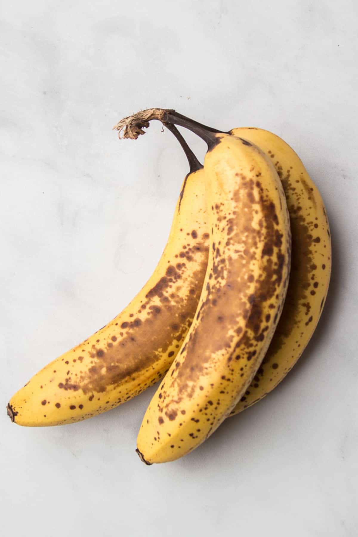 Three overripe bananas sitting on a marble surface.
