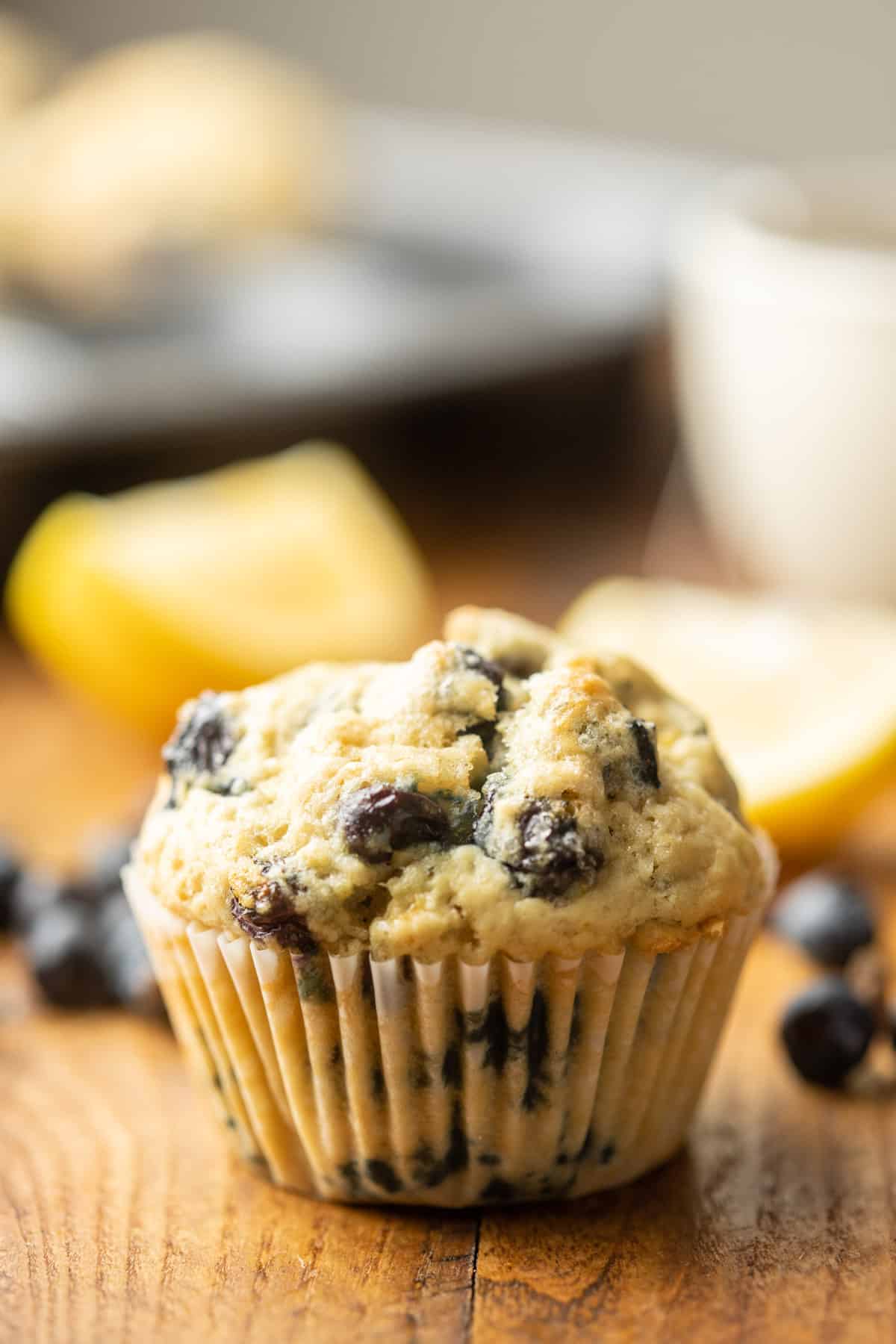 Muffin vegano de arándanos con molde para muffins, taza de té y rodajas de limón en el fondo.