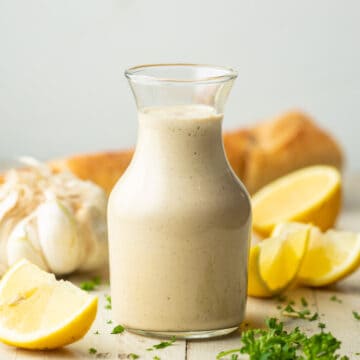Bottle of Vegan Caesar Dressing with garlic, lemon and bread in the background.