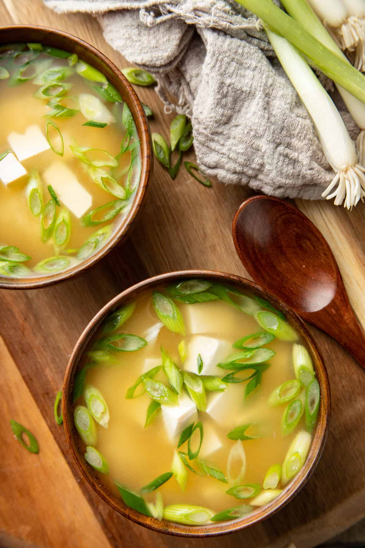 Two bowls of Vegan Miso Soup on a wooden surface with spoon and scallions.
