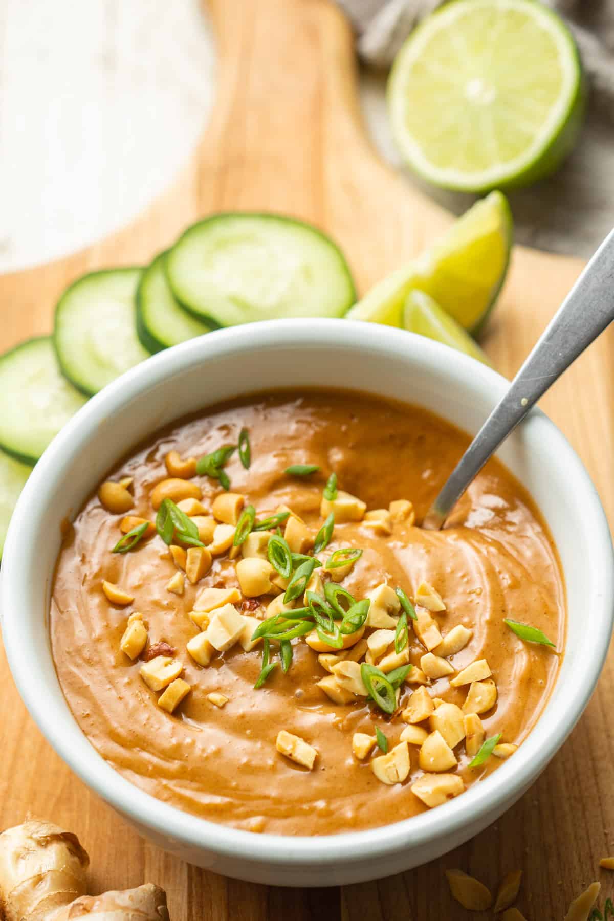 Bowl of Vegan Peanut Sauce with a spoon in it, cucumber slices in the background.