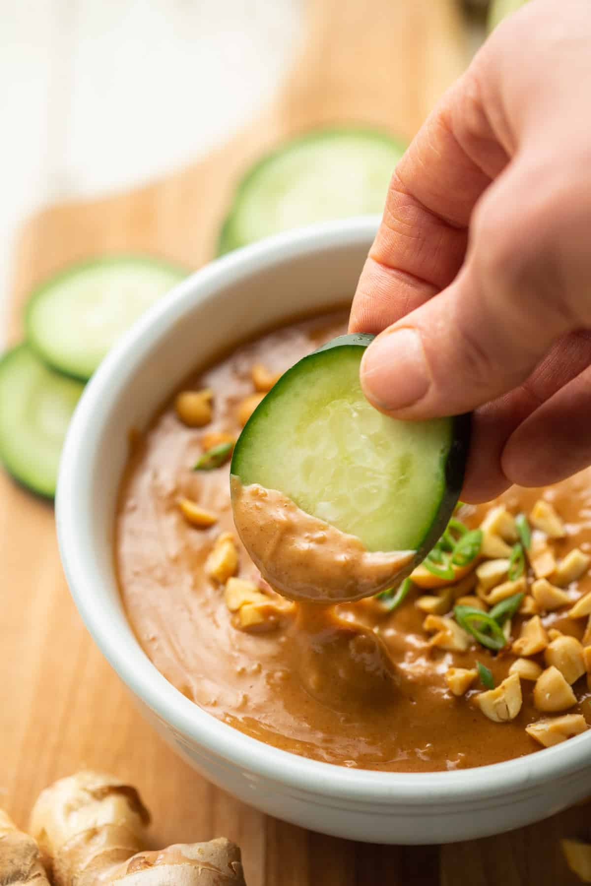 Hand dipping a cucumber slice into a bowl of Vegan Peanut Sauce.