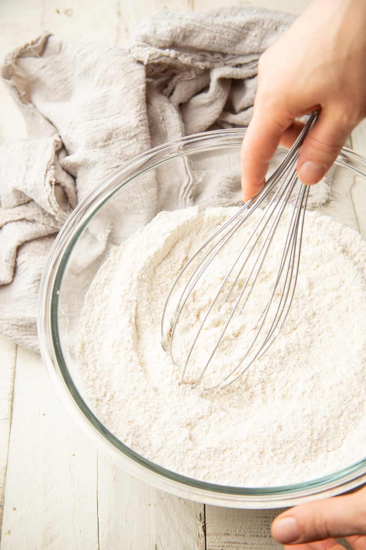 Hand whisking dry cake ingredients together in a bowl.