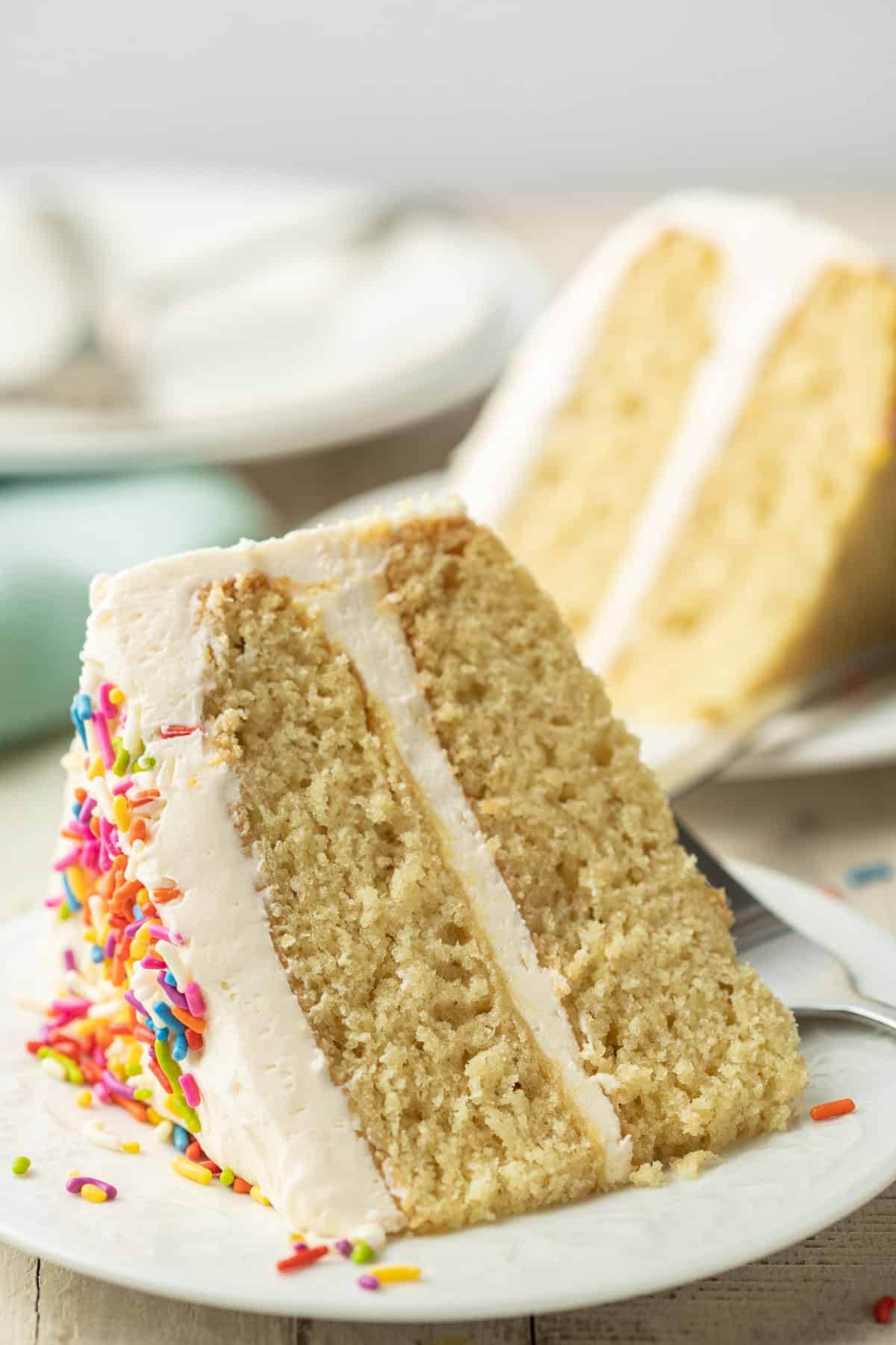 Vegan Vanilla Cake slice on a plate with a second cake slice in the background.