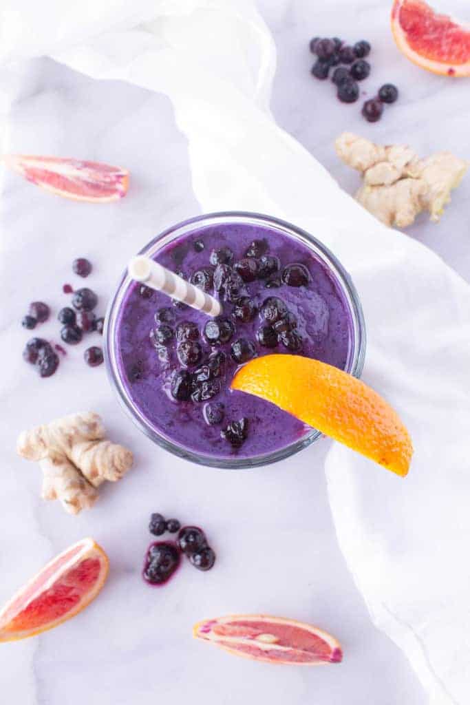 Smoothie in a glass surrounded by scattered blueberries, ginger, and blood orange slices.