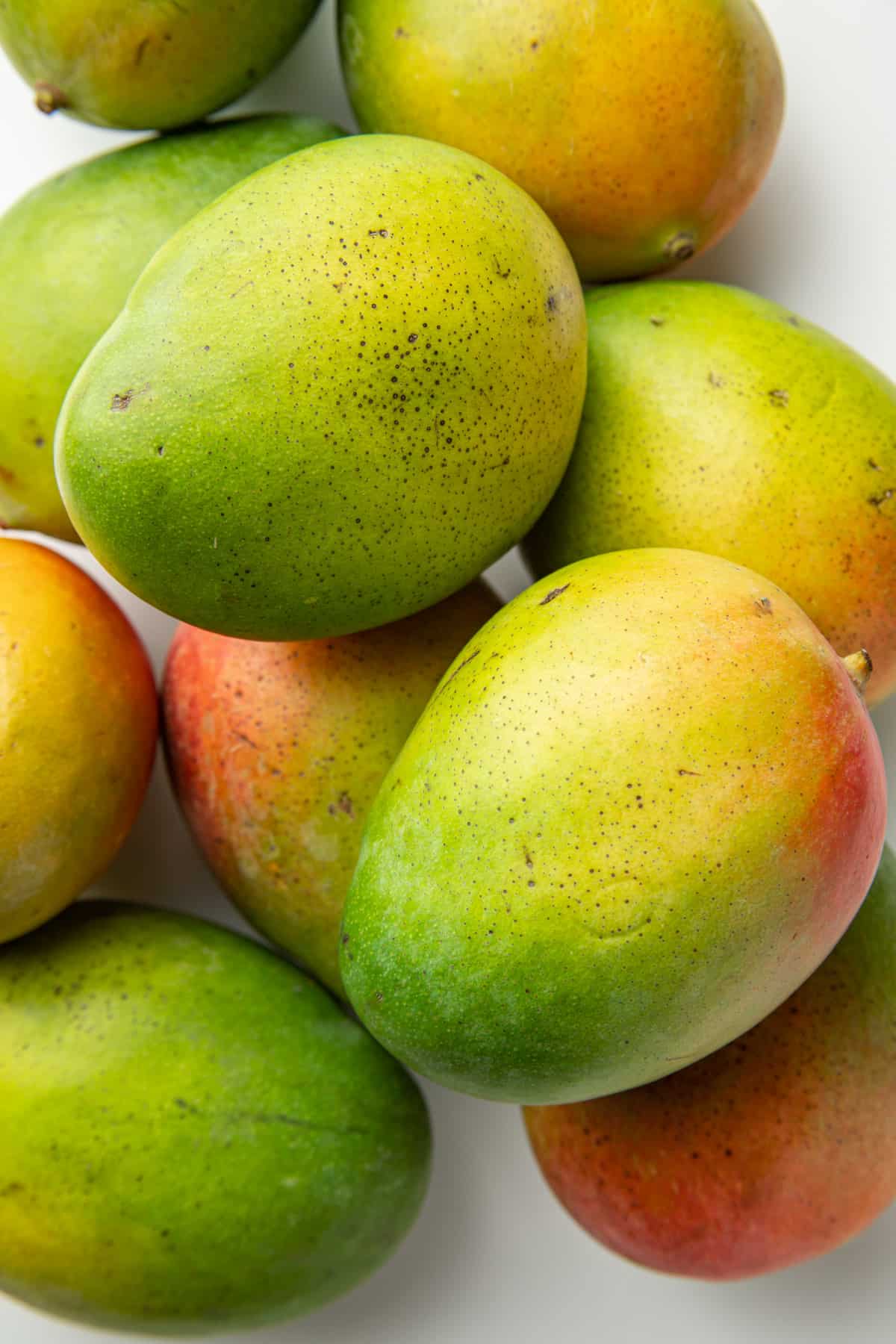 Mangoes piled on top of each other on a white surface.