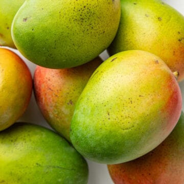 Mangoes piled up on a white surface.