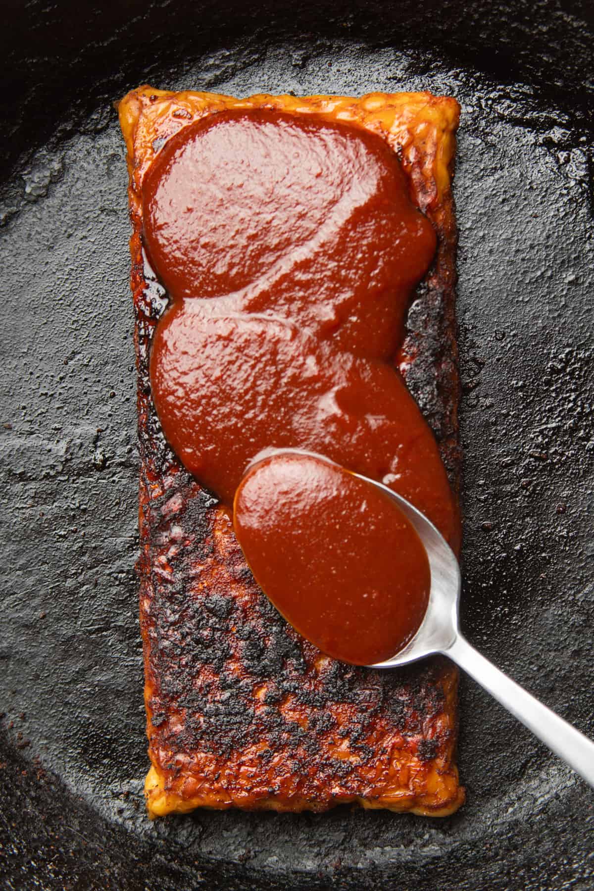 Spoon spreading barbecue sauce on a block of braised tempeh.