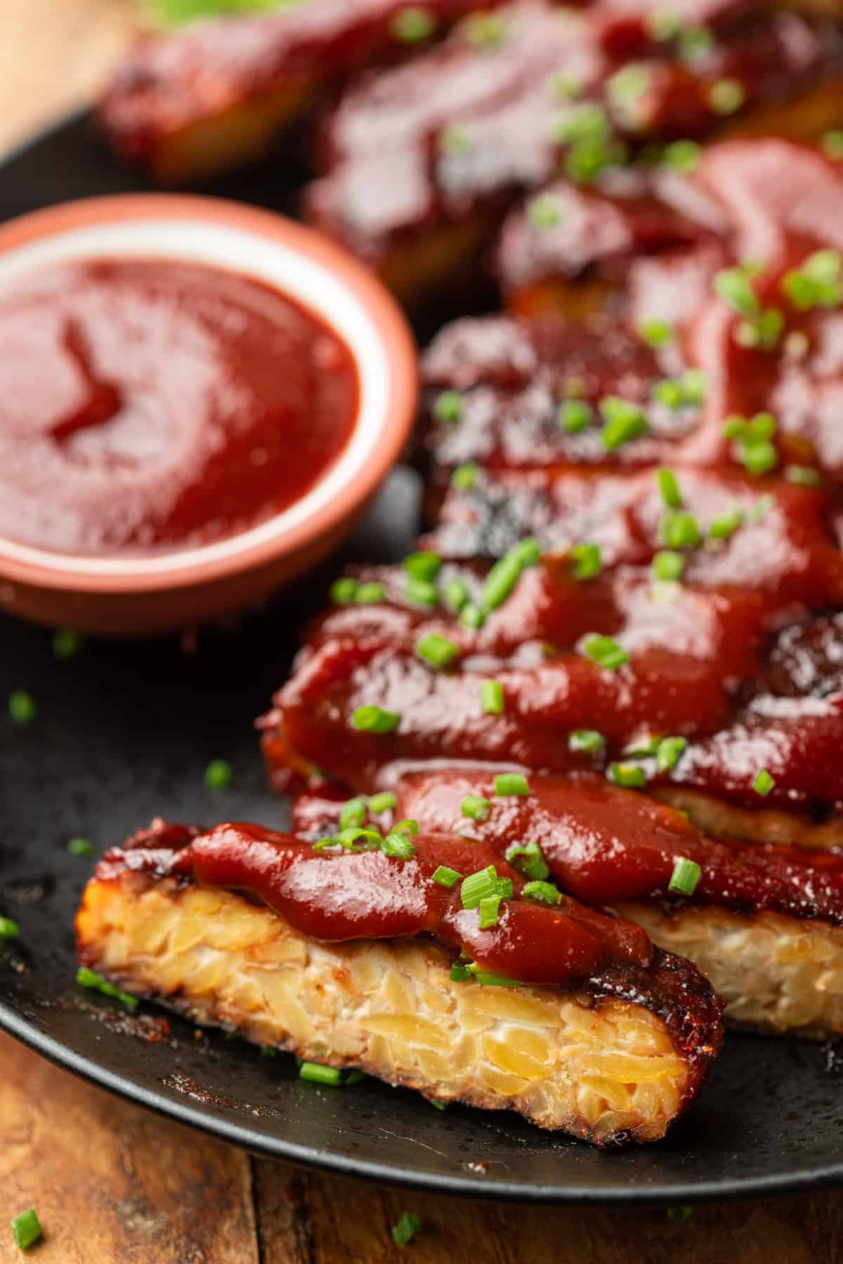 Close up of Tempeh Ribs topped with barbecue sauce and fresh chives.