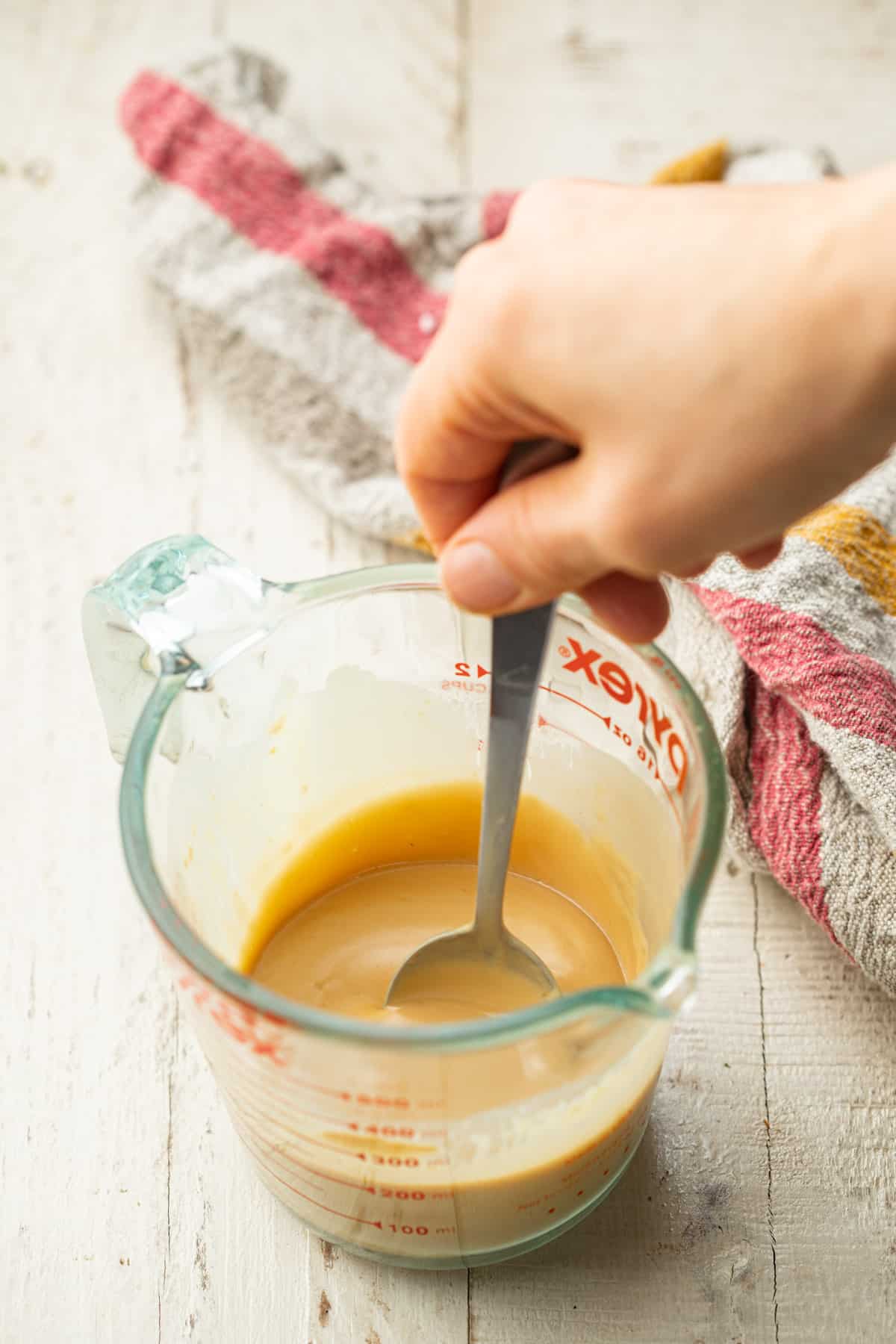 Hand stirring tahini dressing together in a liquid measuring cup.