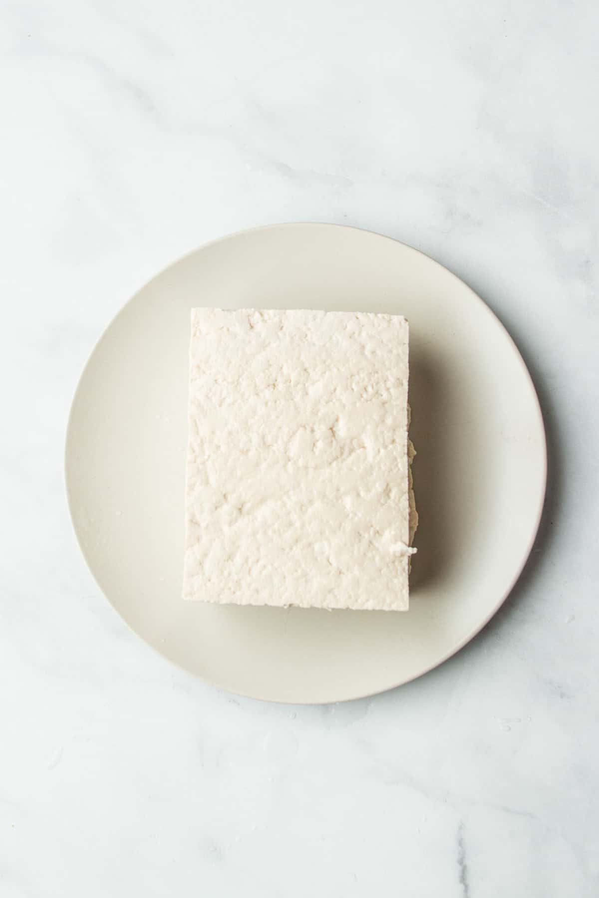 Block of tofu sitting on a white plate.