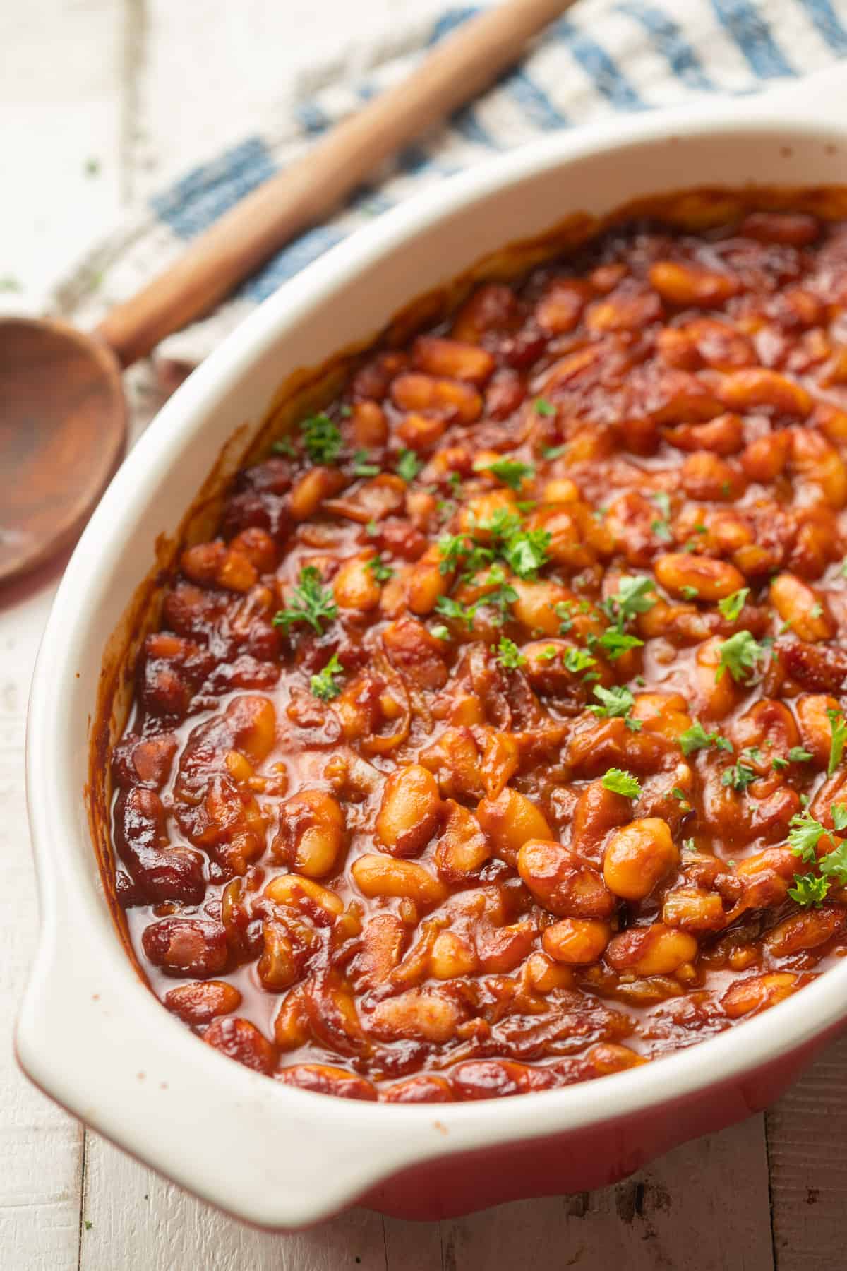 Dish of Vegan Baked Beans with wooden spoon and striped napkin in the background.