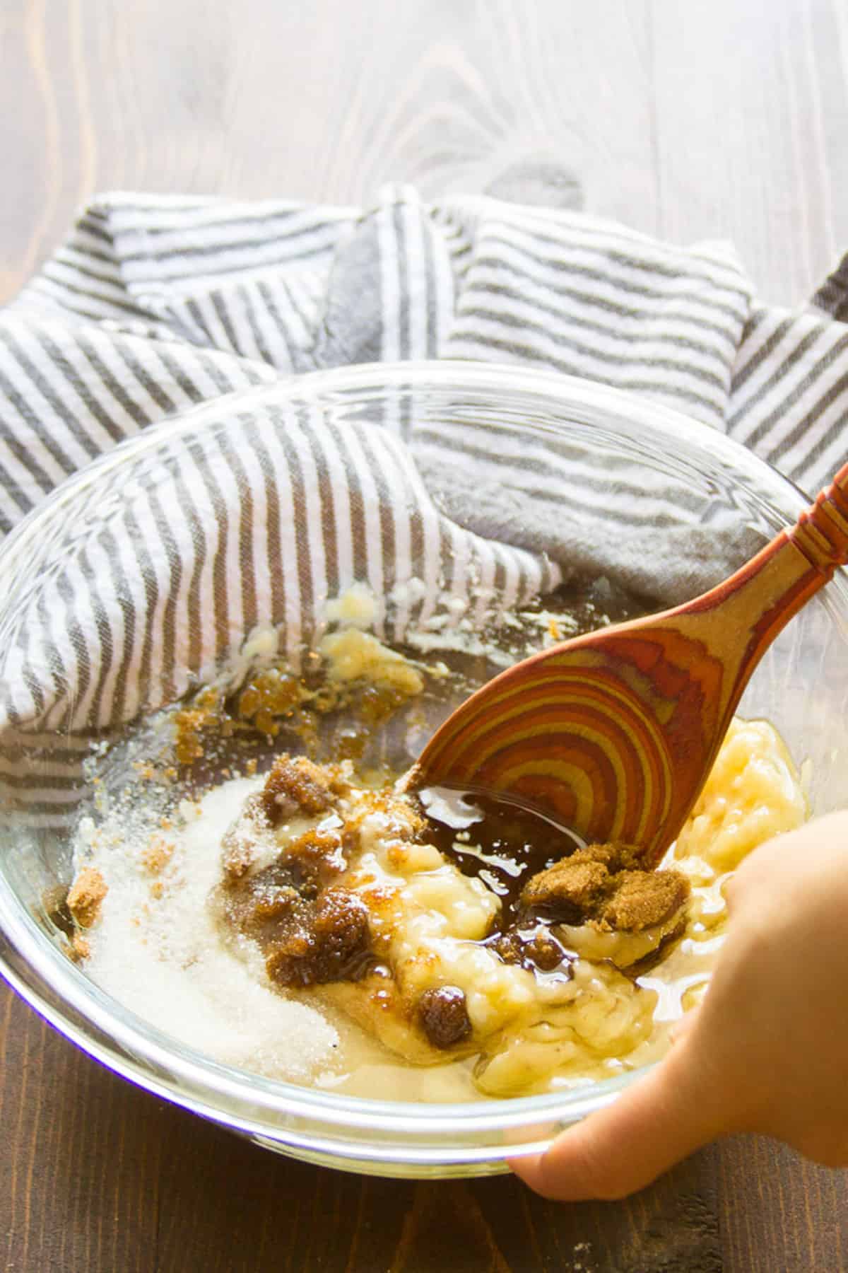 Spoon stirring wet banana bread ingredients together in a bowl.
