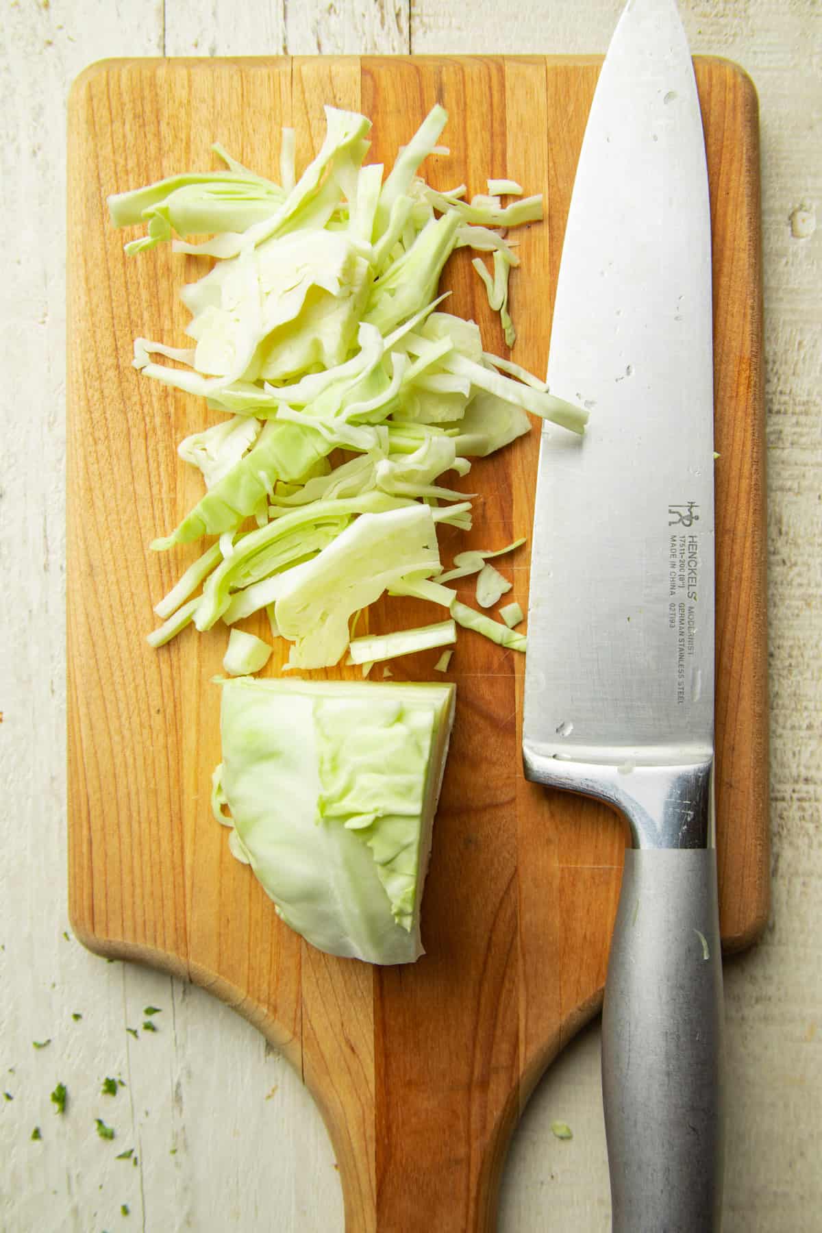 Partially shredded chunk of cabbage on a cutting board with knife.