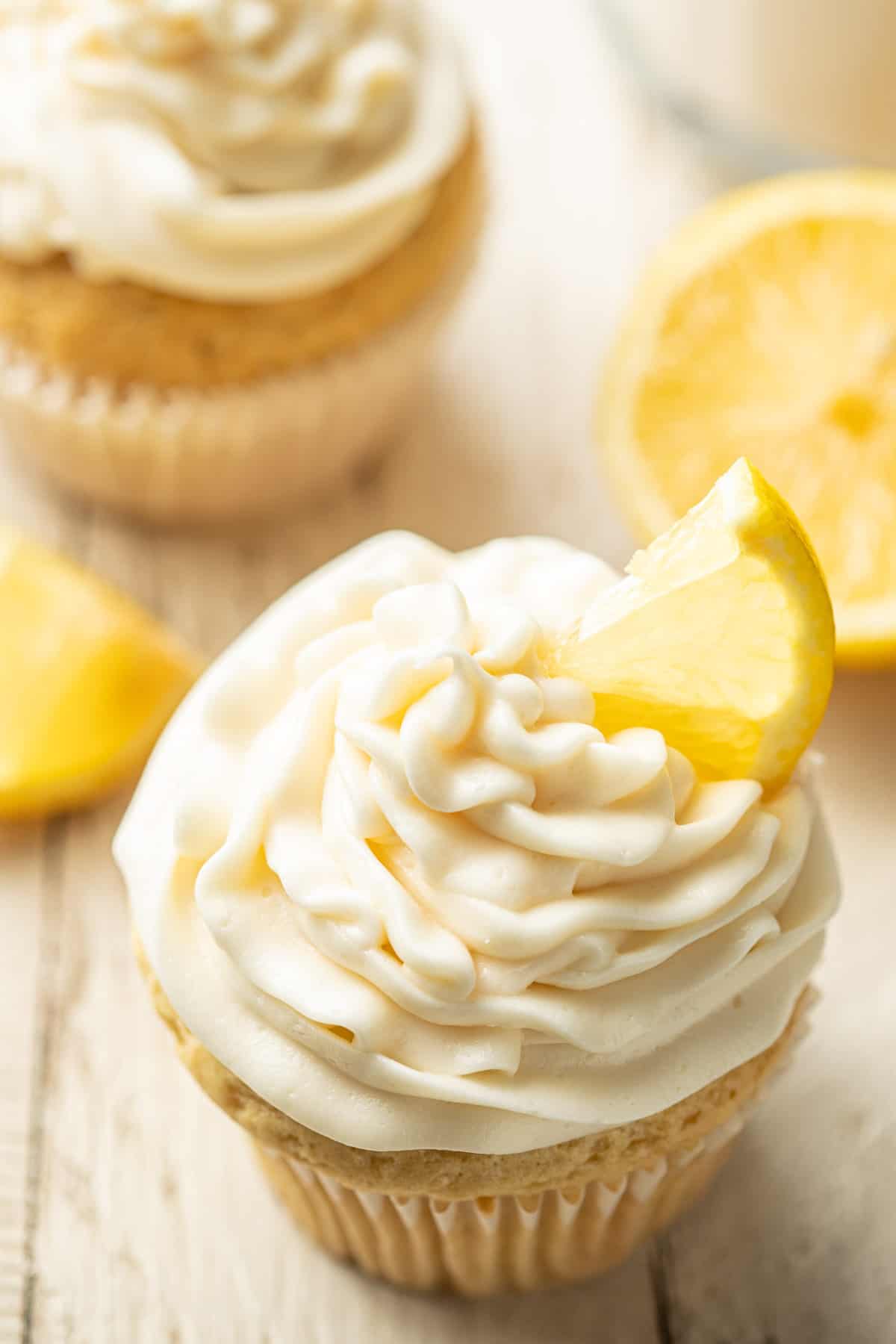 Vegan Lemon Cupcakes on a white wooden surface with lemon slices.