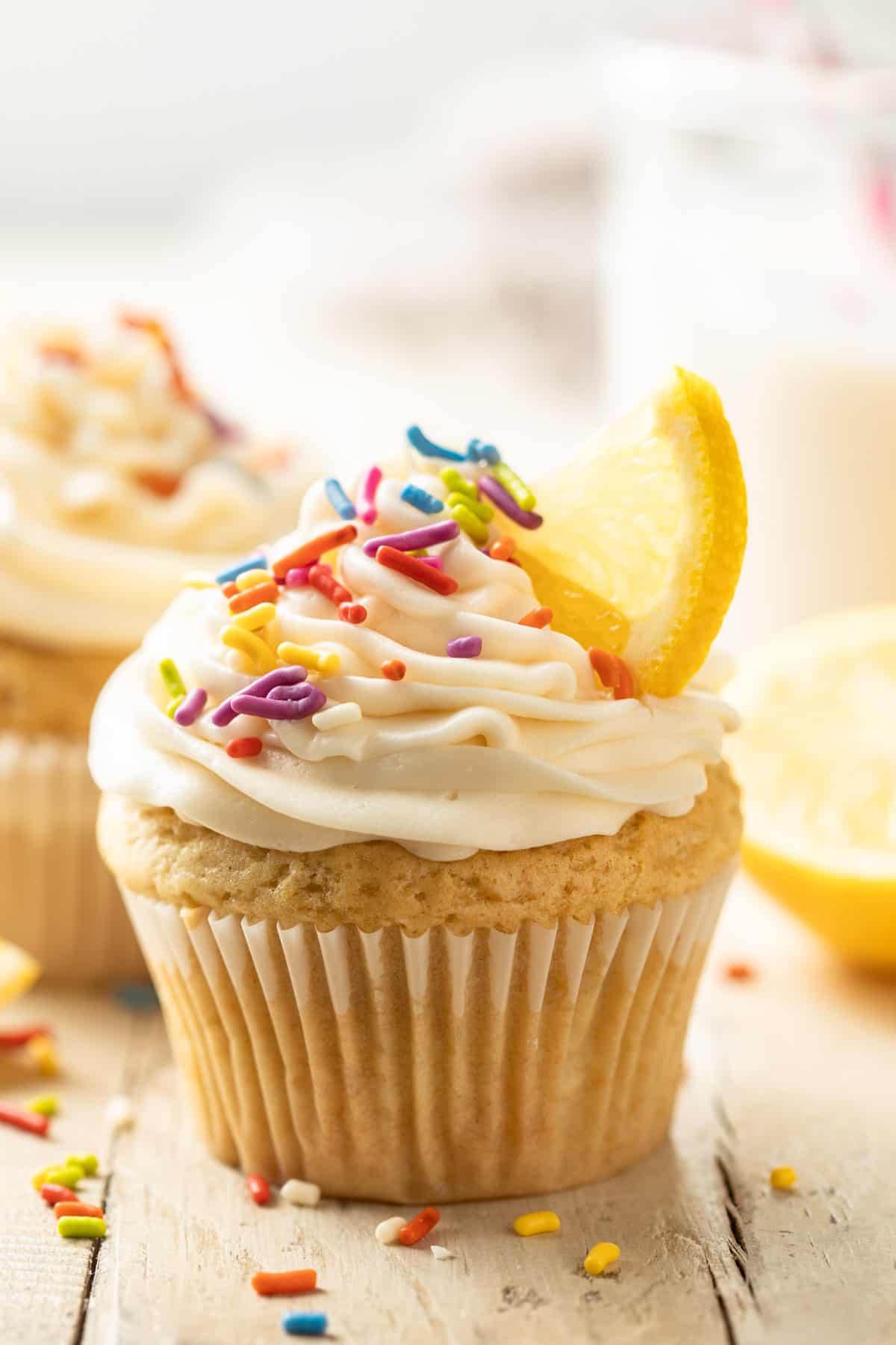 Vegan Lemon Cupcake topped with frosting, rainbow sprinkles, and a lemon slice.