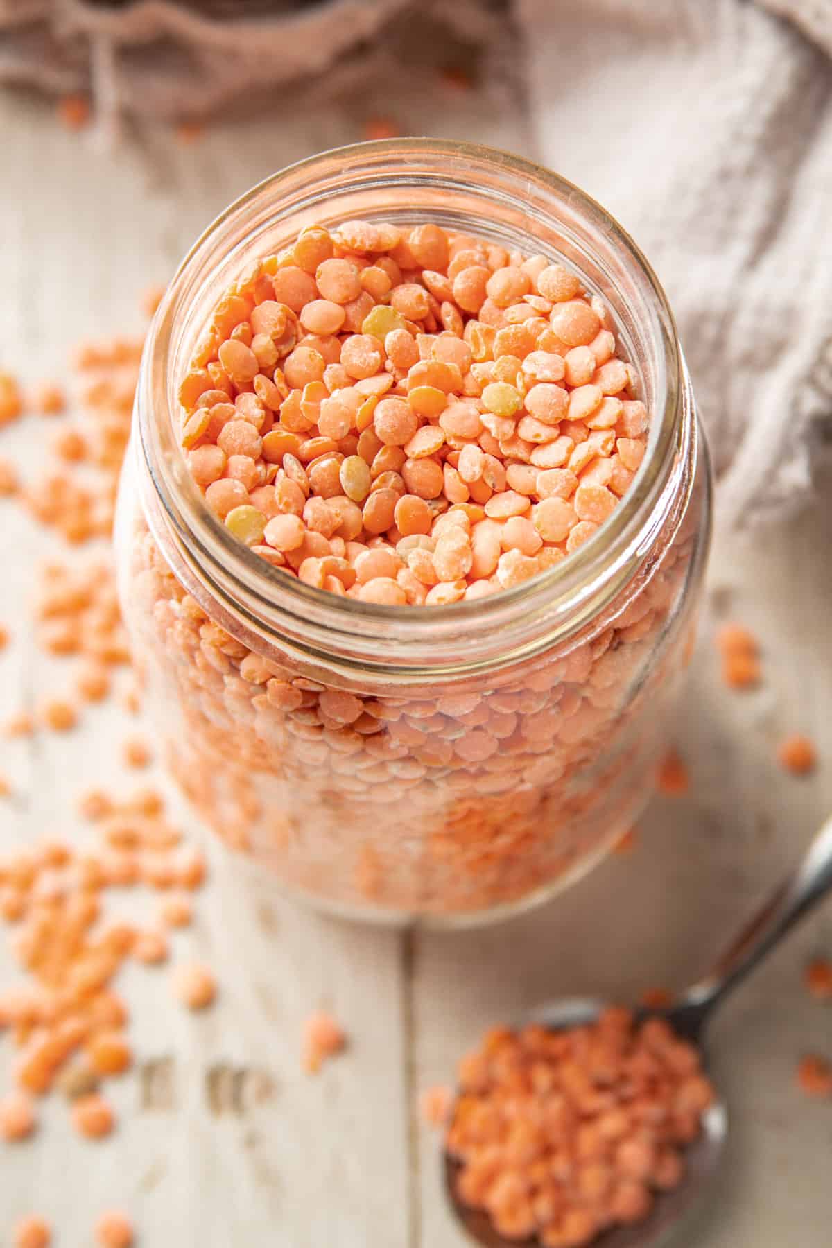 Jar of Red Lentils with spoon and scattered lentils in the foreground.