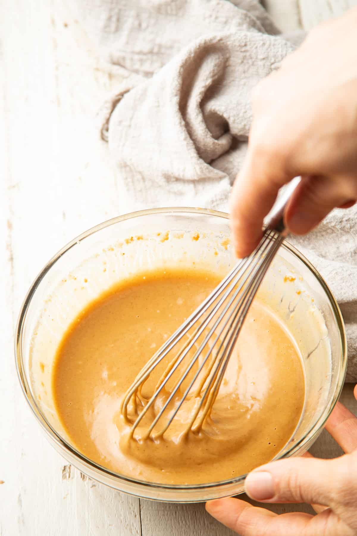 Hand whisking peanut sauce ingredients together in a bowl.