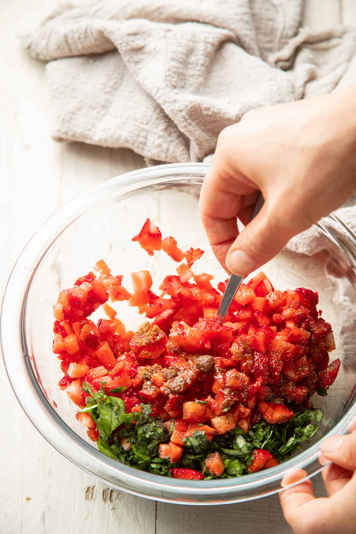Hand stirring Strawberry Bruschetta ingredients together in a bowl.