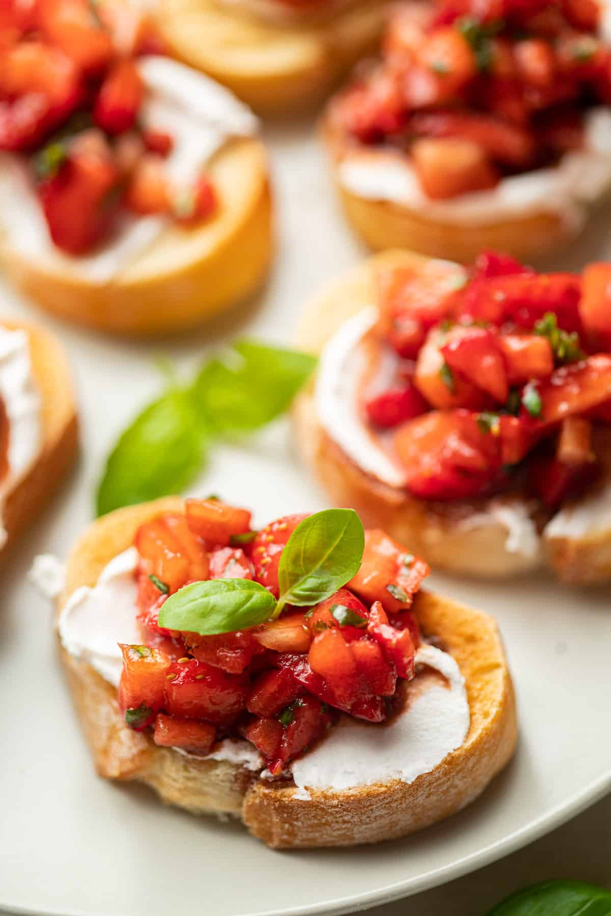 Close up of a baguette slice topped with Strawberry Bruschetta and fresh basil leaves on a plate.