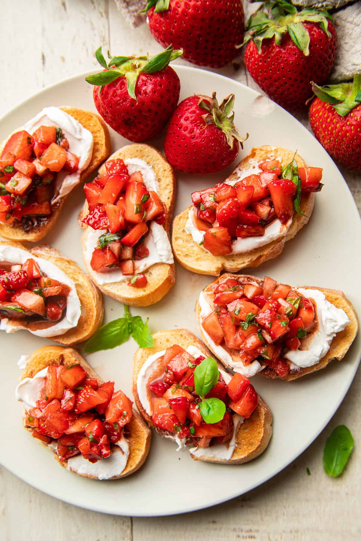 Fresh strawberries and baguette slices topped with Strawberry Bruschetta on a plate.