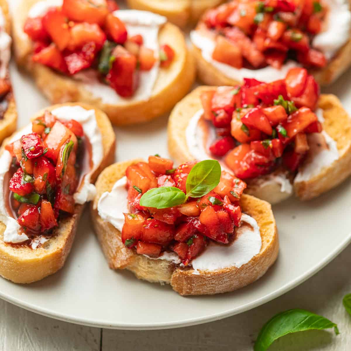 Baguette slices topped with vegan cheese and Strawberry Bruschetta on a plate.