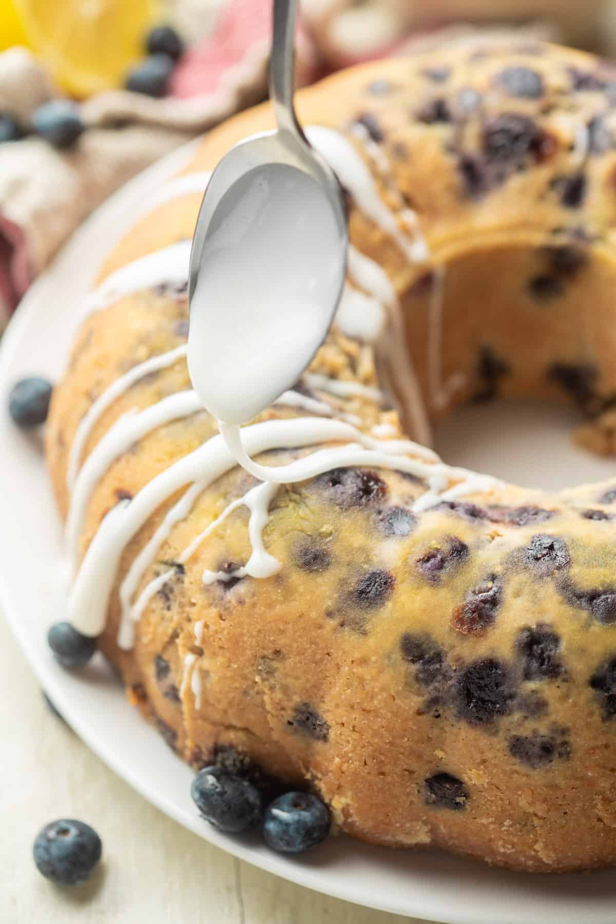 Spoon drizzling glaze over a Vegan Blueberry Cake.