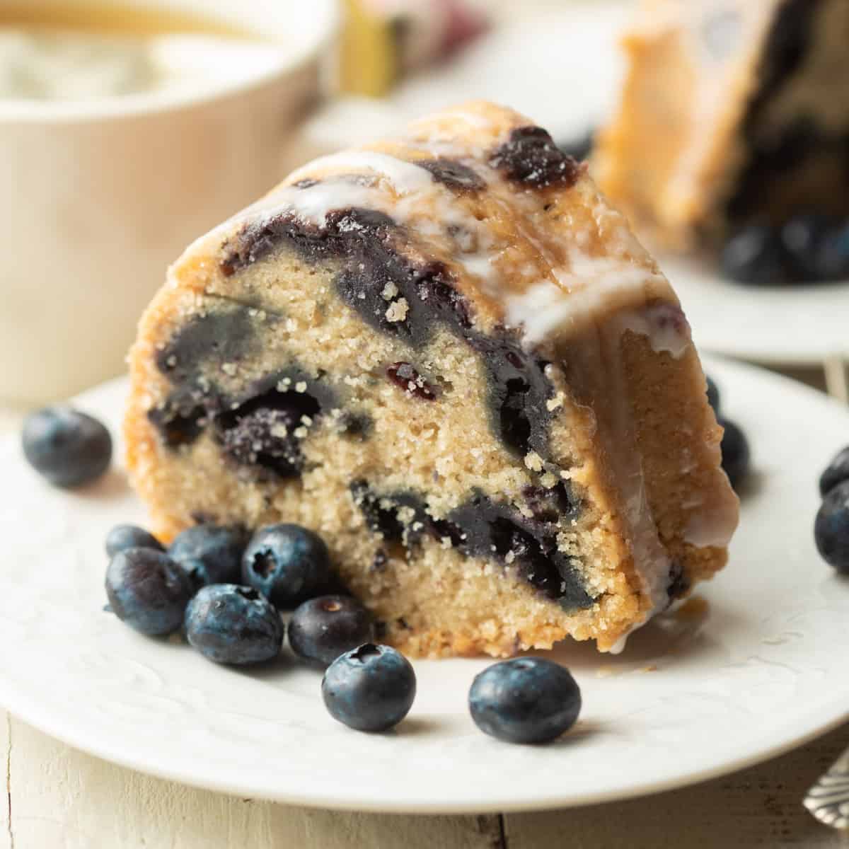 Slice of Vegan Blueberry Cake on a plate with fresh blueberries.