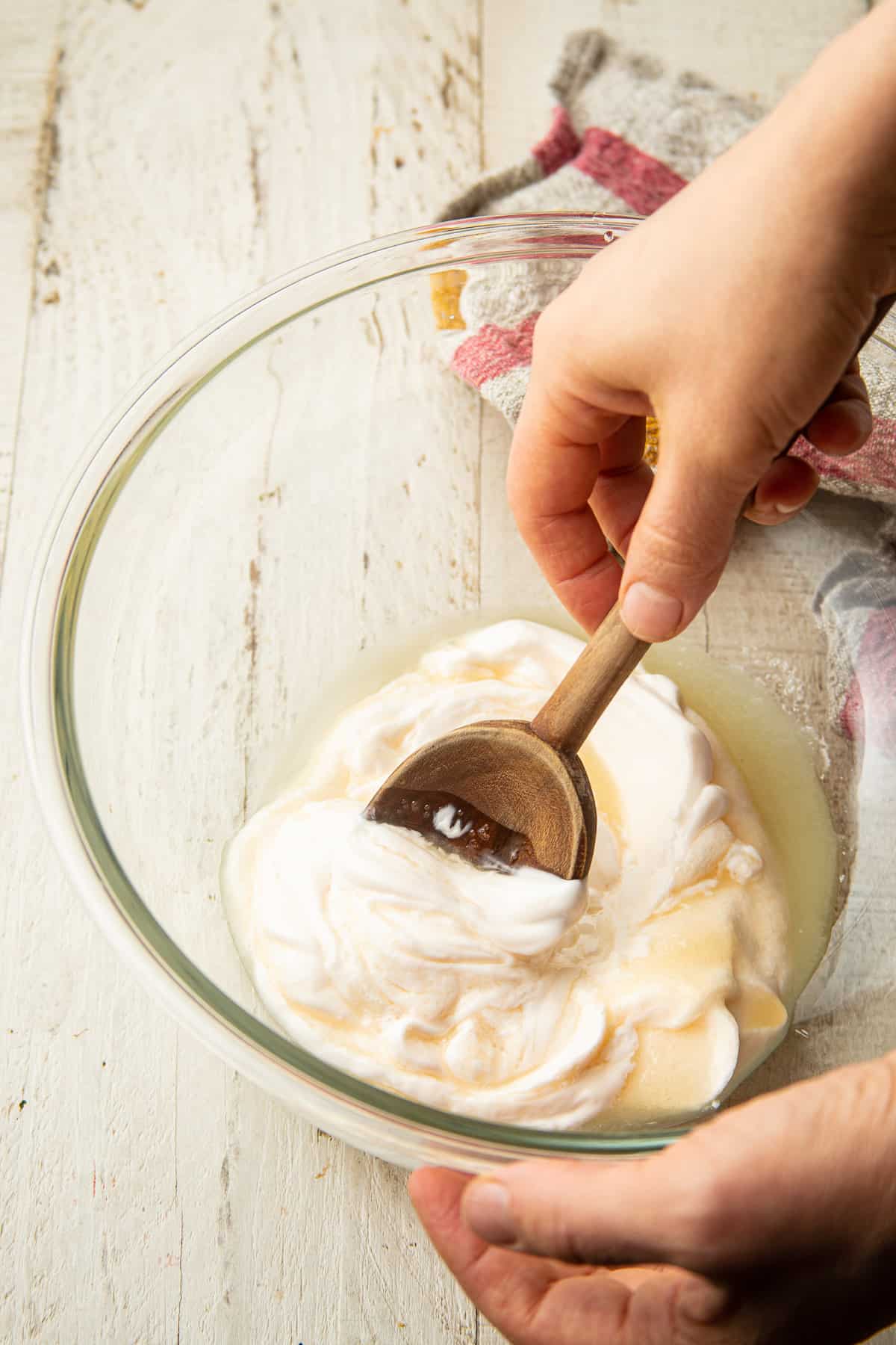 Hand stirring mayo, vinegar, and sugar together in a glass bowl.